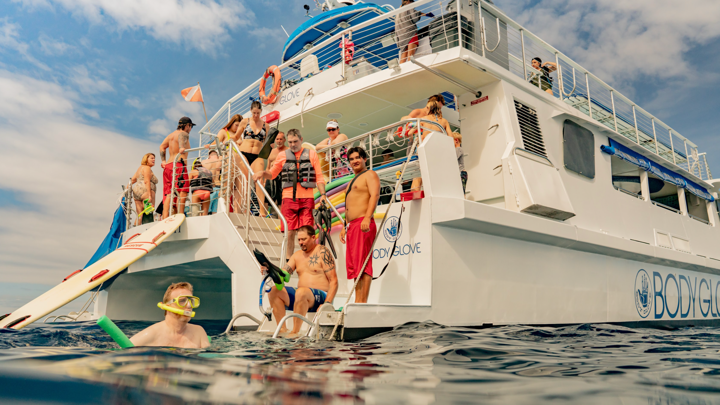 group of people standing at the back of the boat with some people in the water