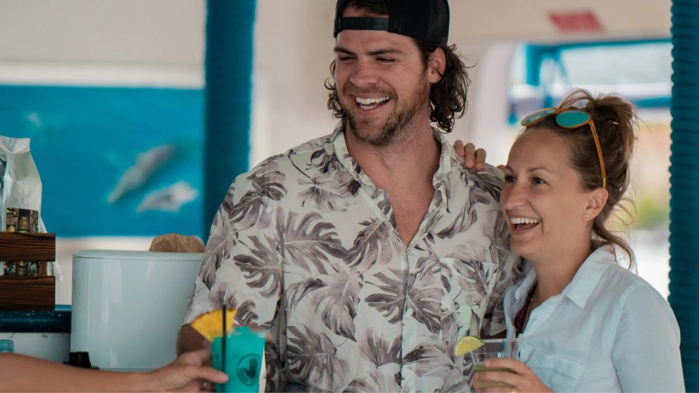 A man and woman smiling and holding drinks while on a sunset dinner cruise from kona