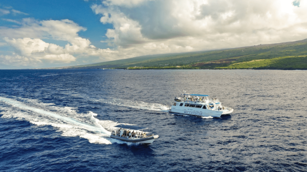 Two boats on blue ocean with cloudy sky and green island coastline in background.