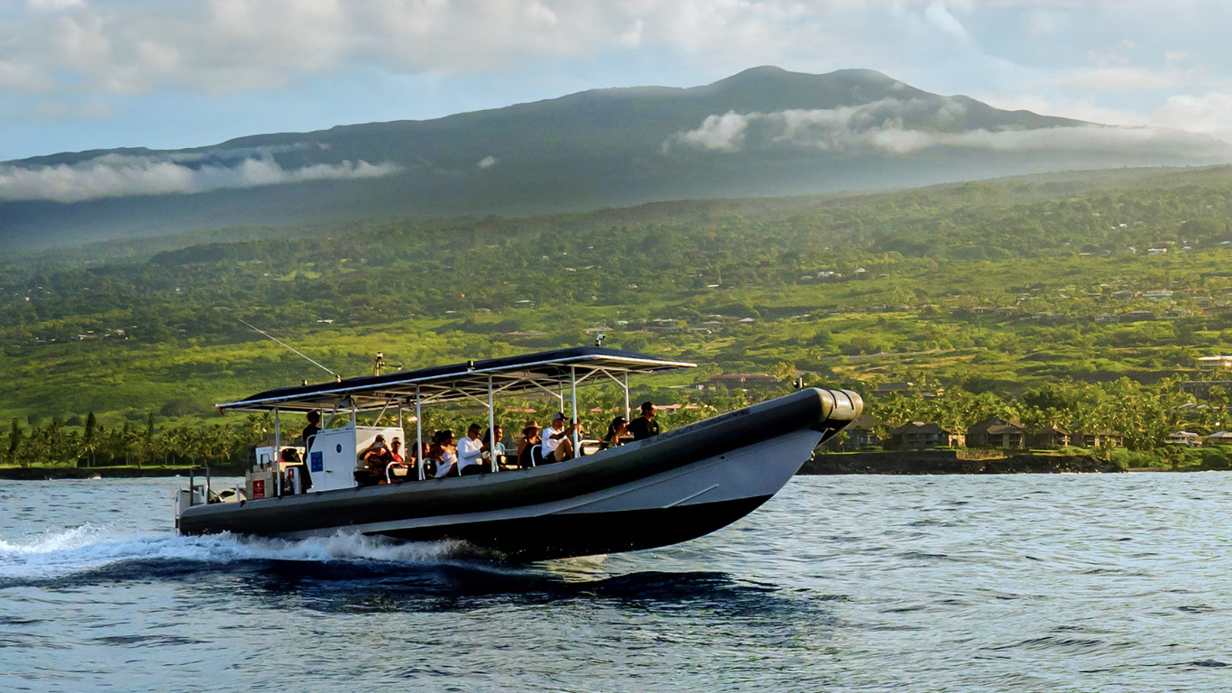 super raft with passengers cruising near lush green mountains under a blue sky on a snorkel tour in hawaii
