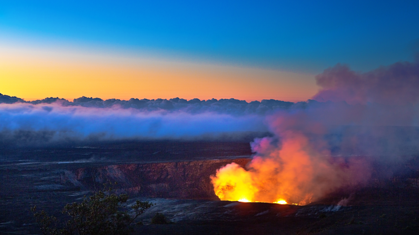 Sunset over a volcanic crater emitting bright lava and smoke with a colorful sky in hawaii volcanoes national park