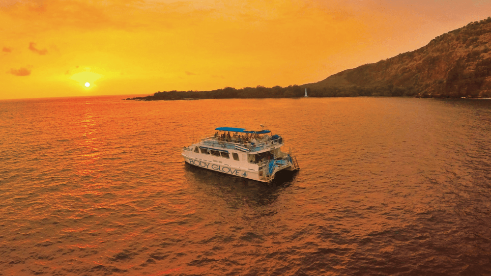 Boat on orange sea at sunset near mountainous coastline.