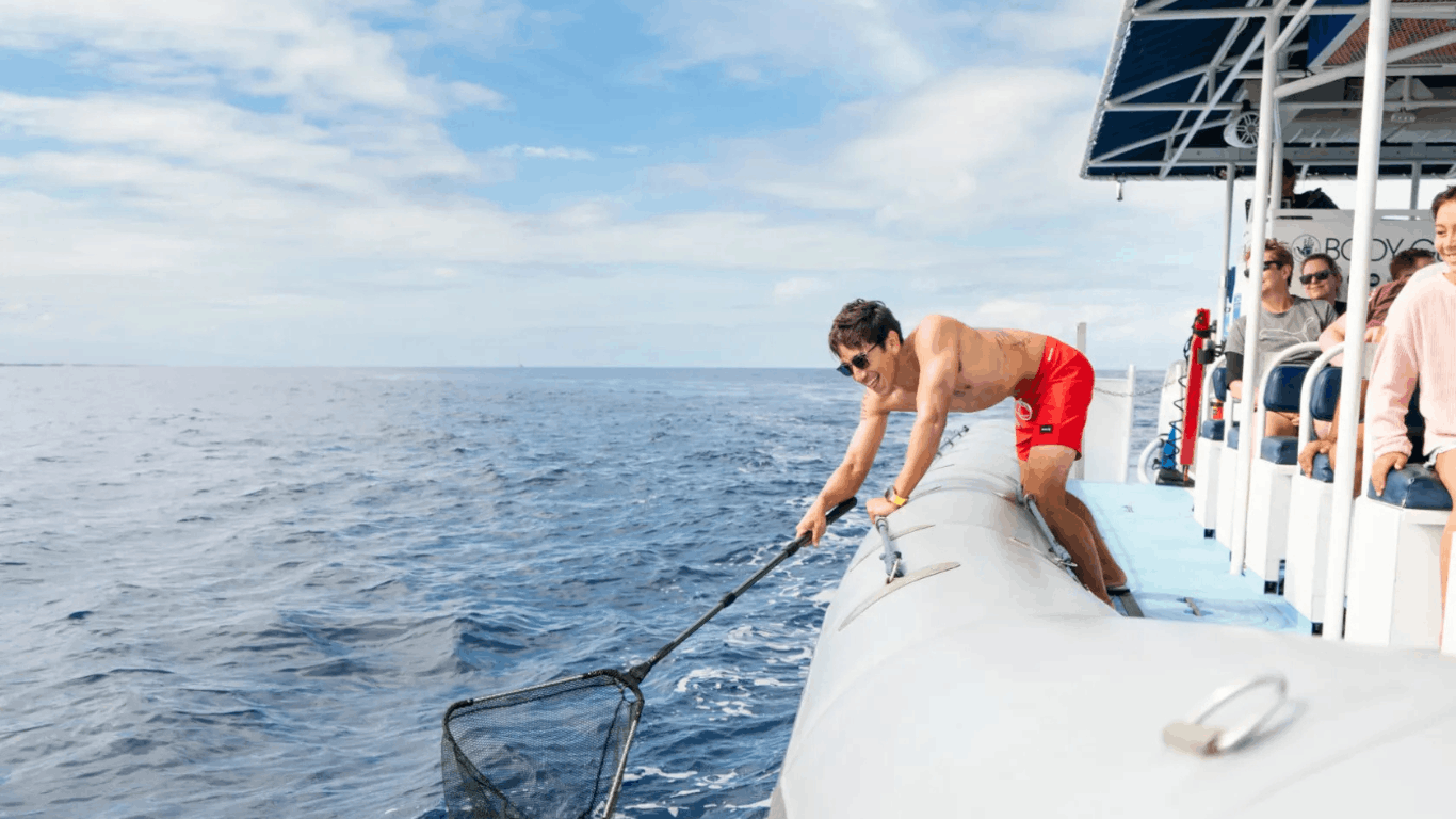 Person on boat using net to scoop something from the ocean on a kona hawaii marine debris clean up