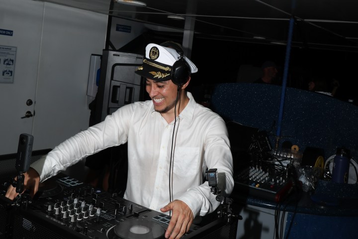 Man in captain's hat DJing with equipment in dimly lit room.