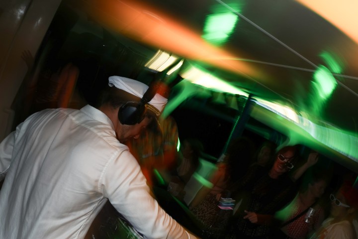 DJ wearing headphones performing at lively party with colorful lights.