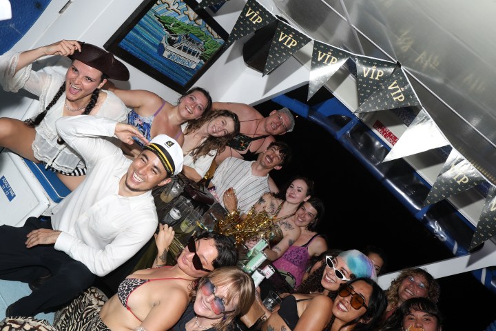 Group of people partying on a boat, some wearing sunglasses, with 'VIP' banner above.