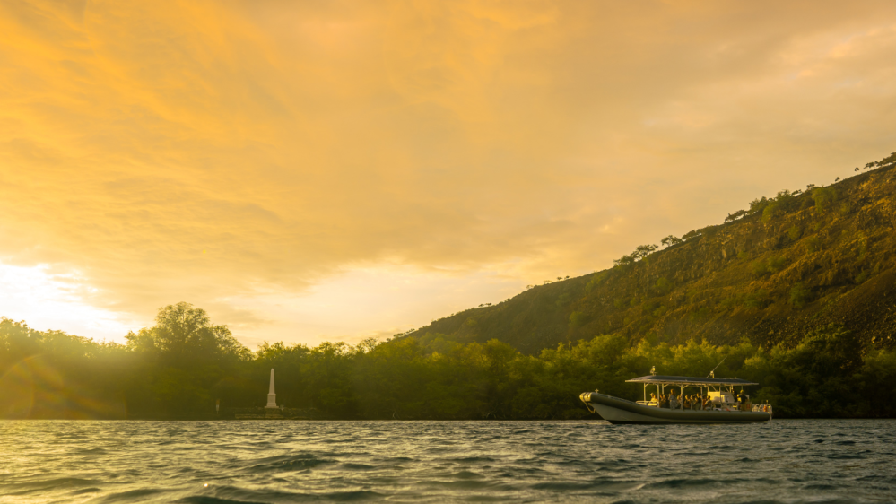 Boat on water near the kona coast at sunset with orange sky.