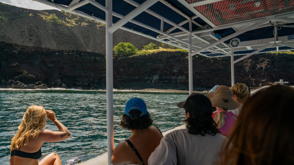 Group of people on a boat near the hawii coastline with greenery.