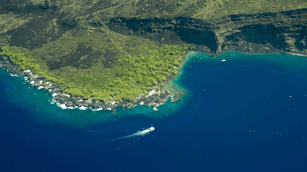 Aerial view of a lush coastal area with turquoise waters and a boat cruising to kealakekua bay