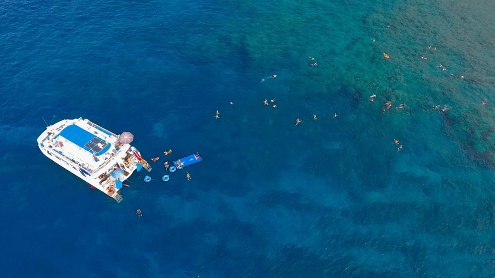 Aerial view of a boat with people swimming in the ocean.
