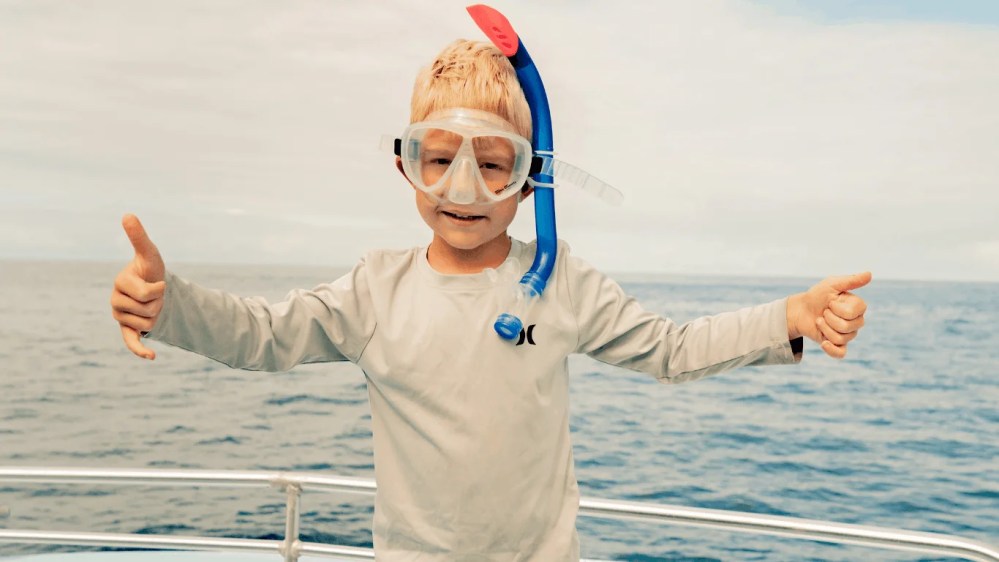 Child in snorkel gear giving thumbs up on a snorkel tour out of kona