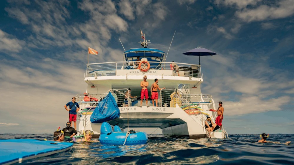 People on a boat enjoying the Kona coast, with some snorkeling and relaxing on floats.